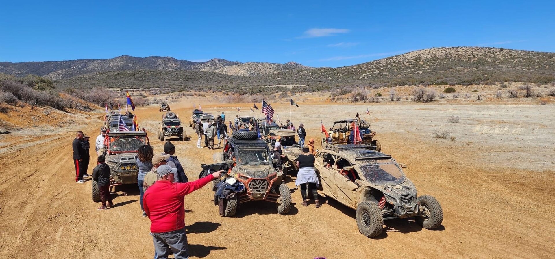 A group of people standing around parked off road vehicles.