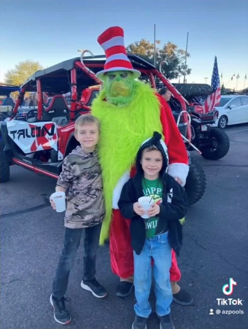 A man dressed as the grinch poses with two children.