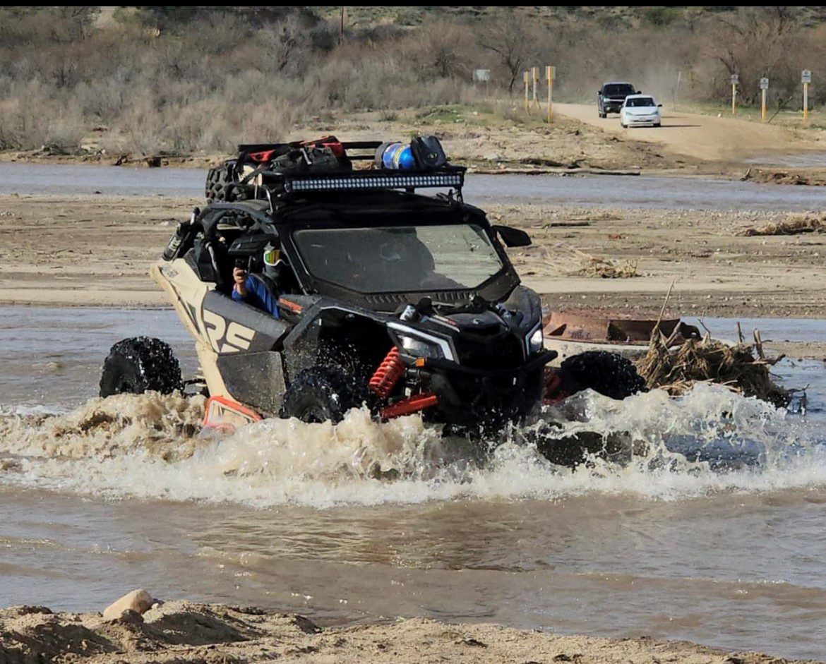 A black vehicle is driving through water on the beach.