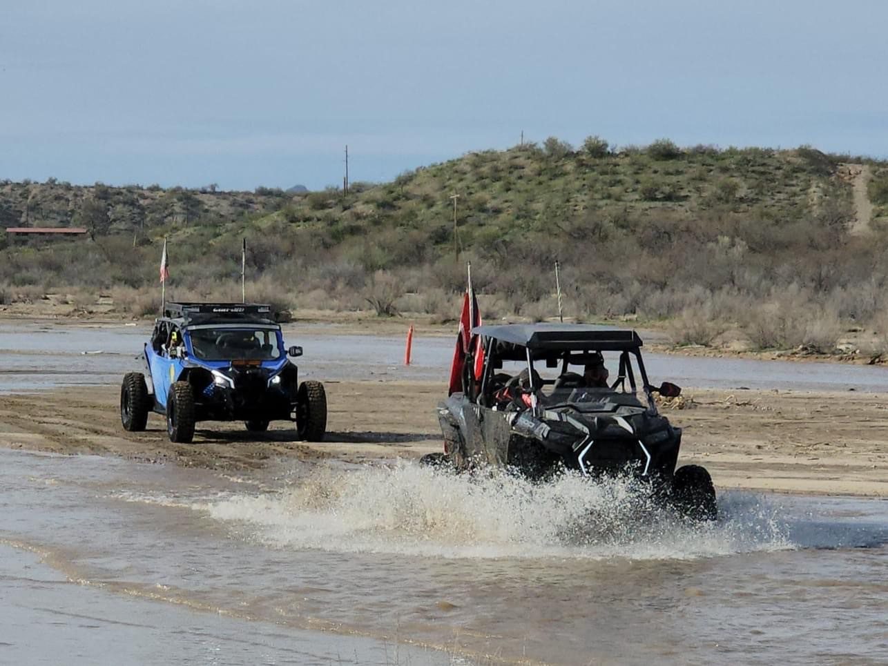 Two vehicles driving through water on a dirt road.