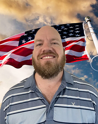 A man with a beard and striped shirt in front of an american flag.