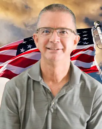 A man with glasses and an american flag in the background.