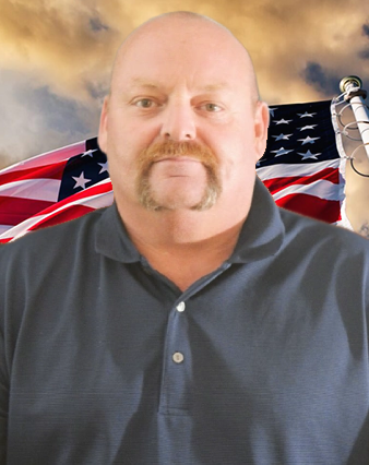 A bald man with a microphone and an american flag in the background.