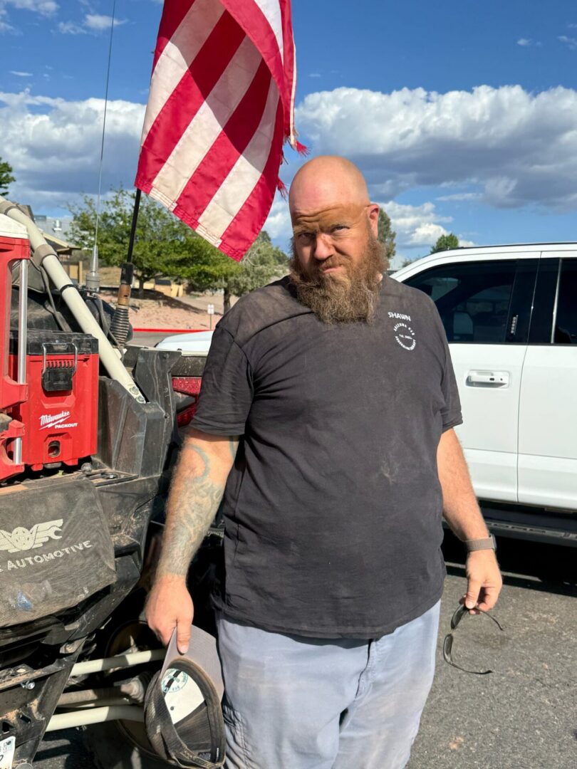 Bearded man standing by vehicles, American flag