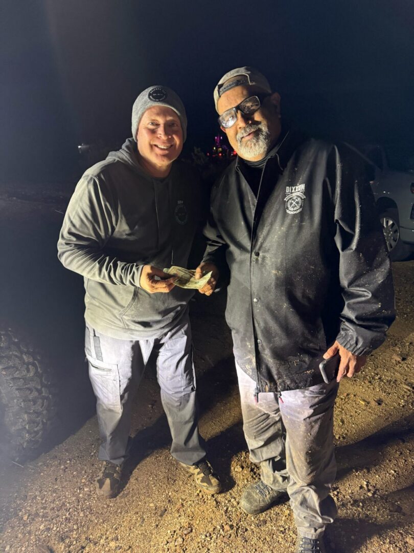 Two men smiling, holding cash at night