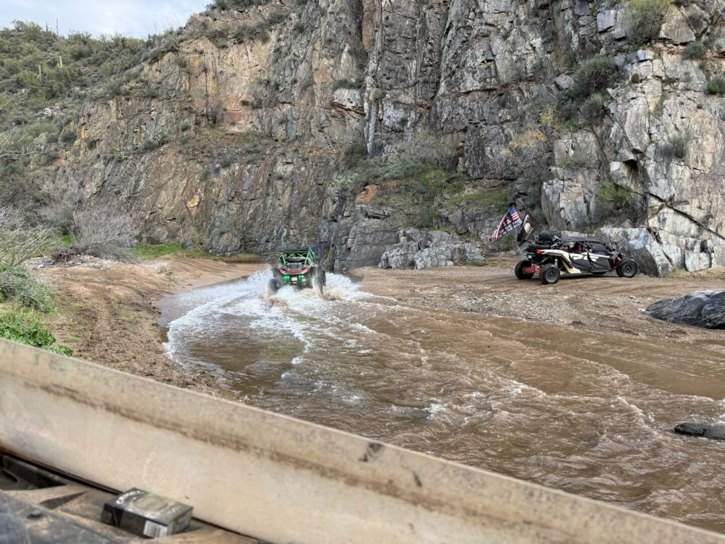 UTVs crossing muddy stream in rocky canyon