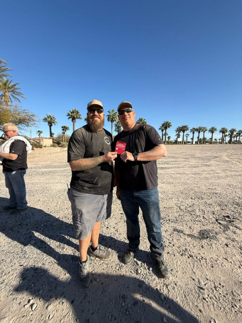 Two men holding red pass under palm trees