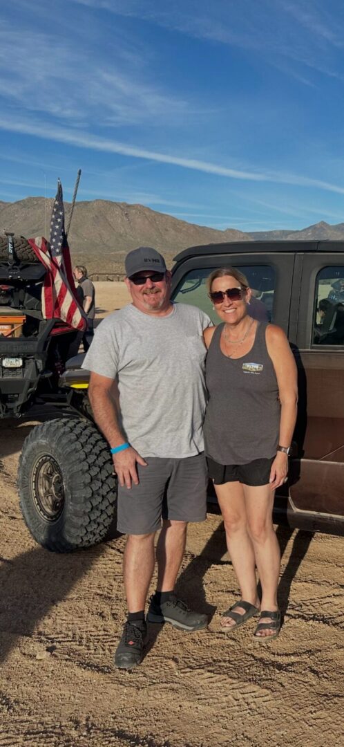 Two people posing beside off-road vehicle in desert