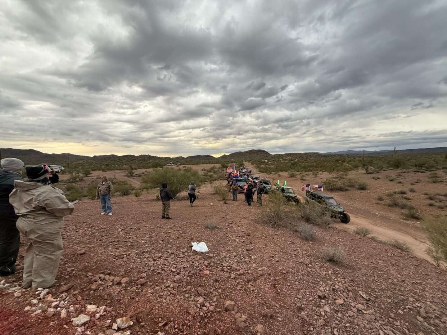 Off-road vehicles and spectators under cloudy desert sky