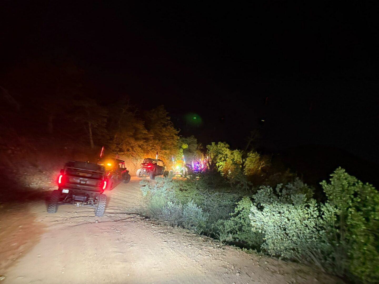 Vehicles on dirt road at night with lights