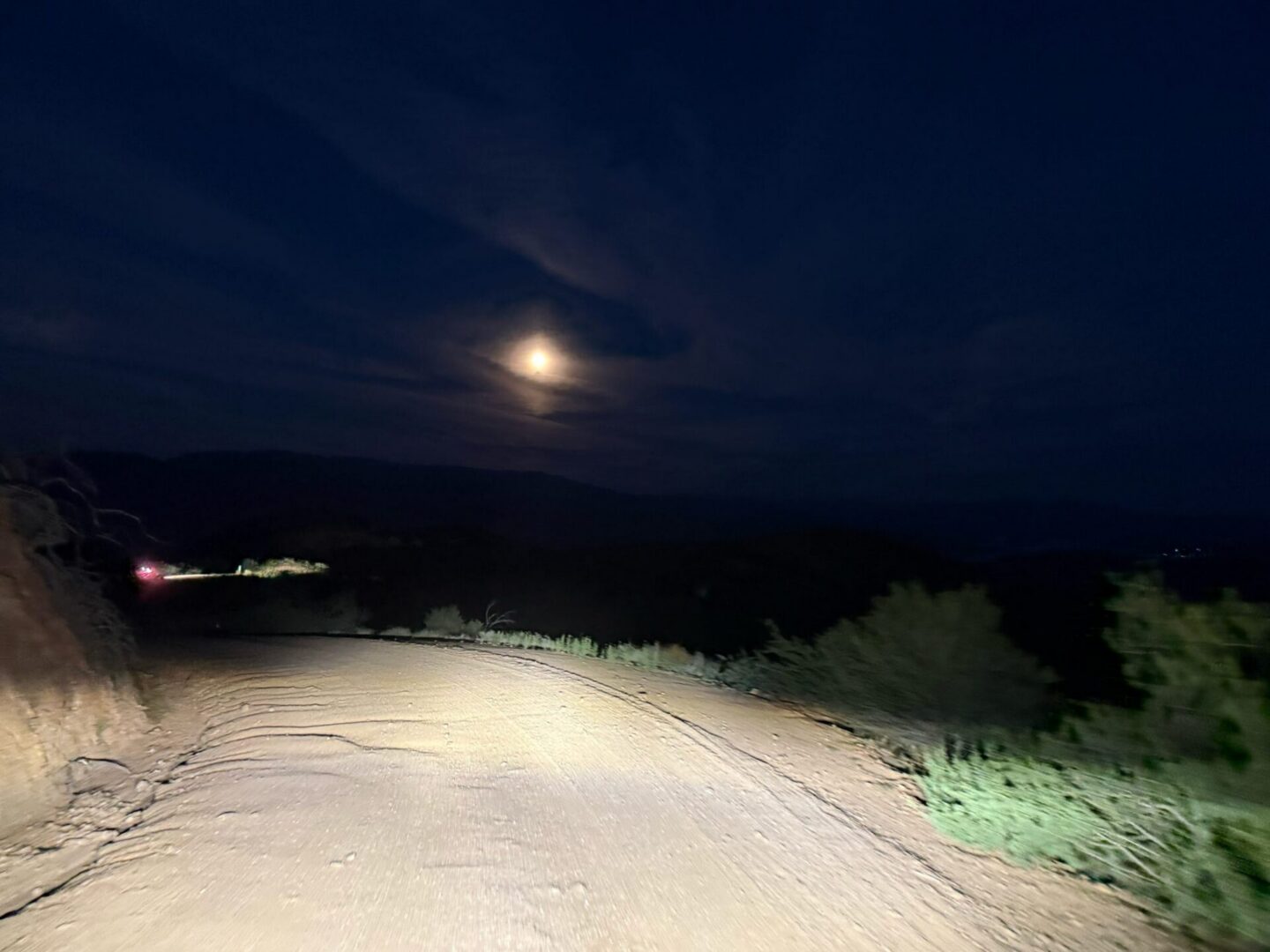 Car headlights on moonlit dirt road