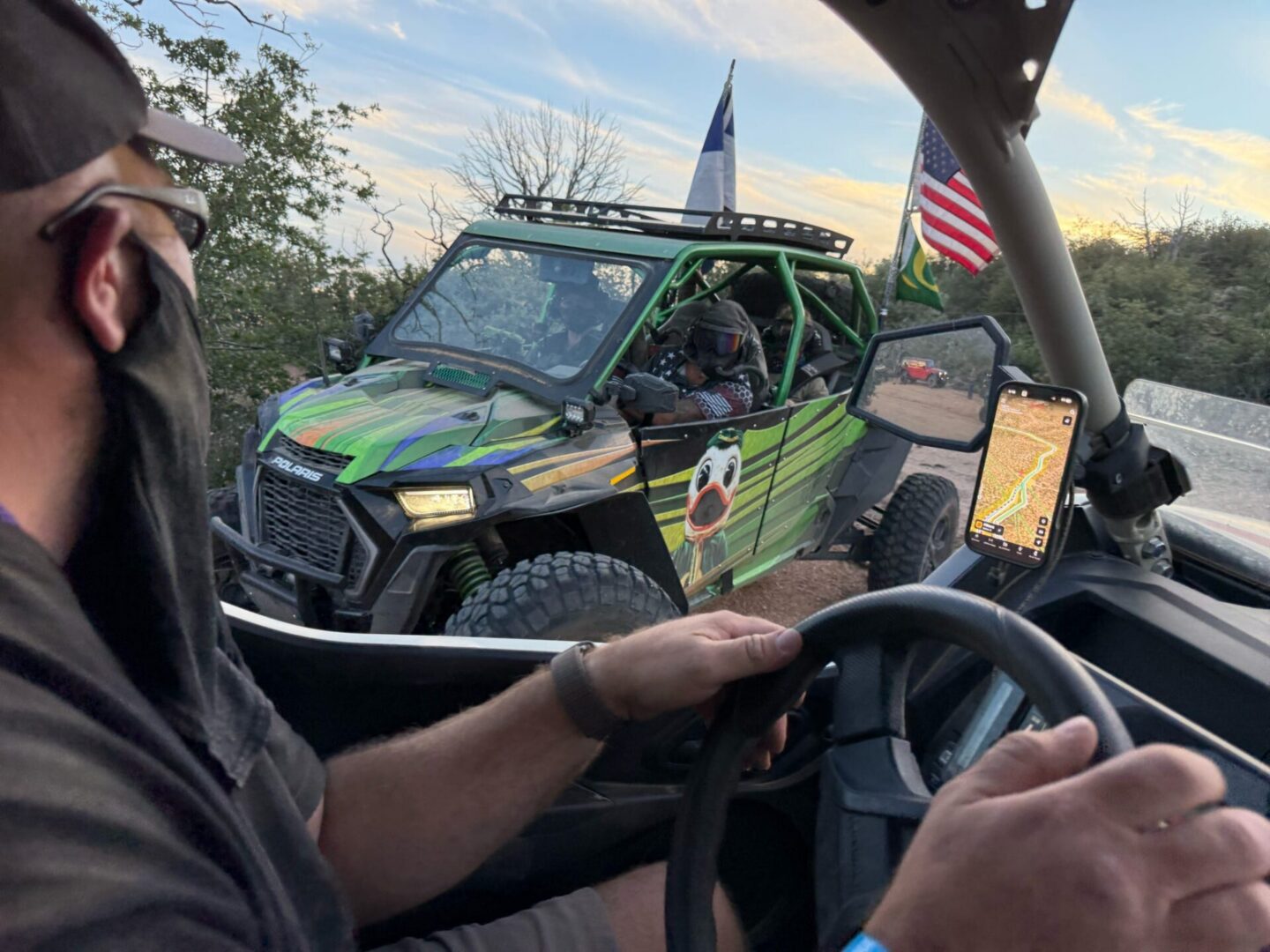 Masked driver steering, green UTV with flags passes