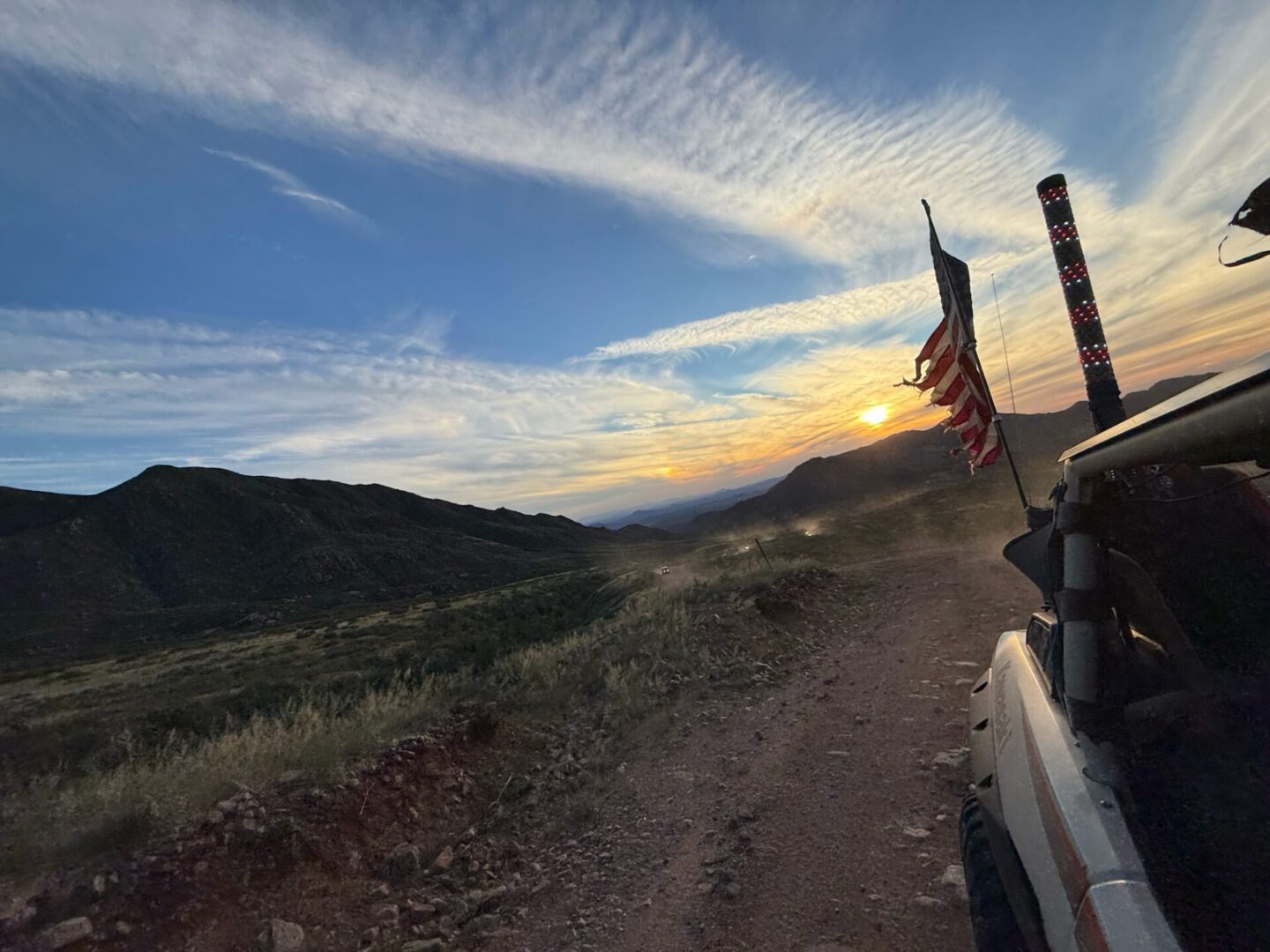 Off-road vehicle with flags driving at sunset