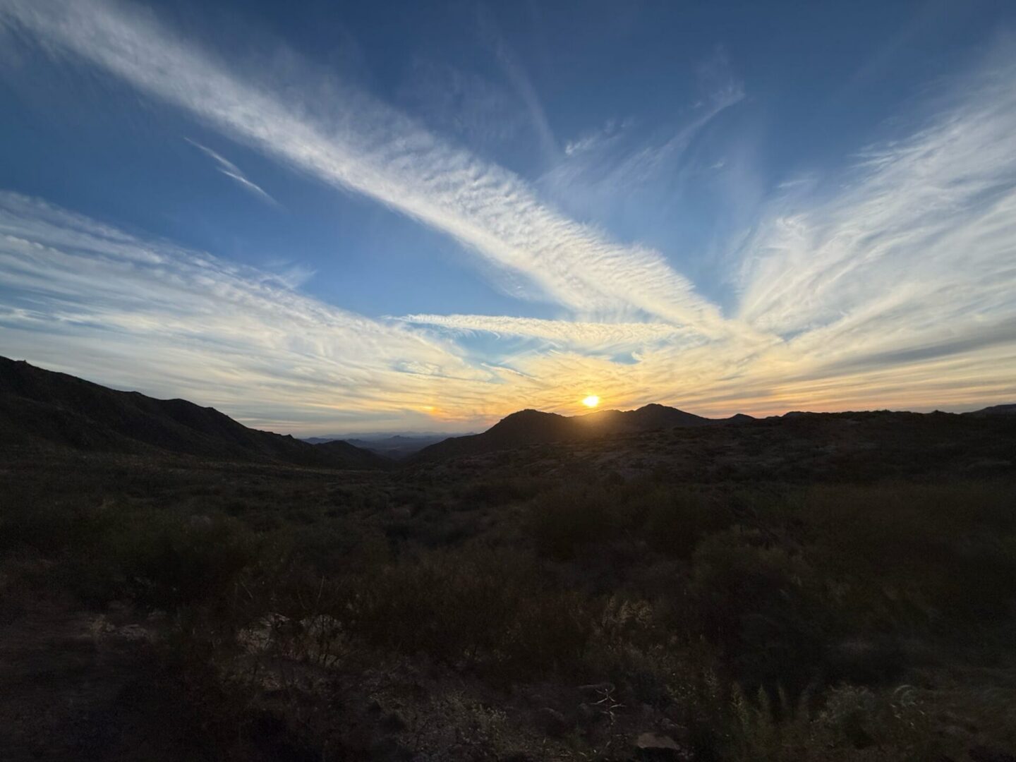 Sunset over rolling hills with streaked clouds