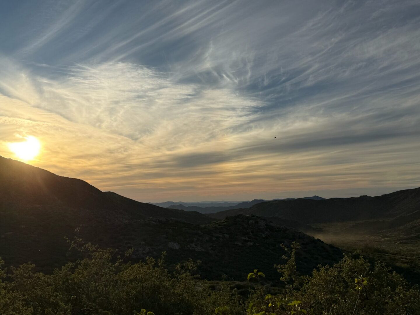 Sunset over mountainous valley with wispy clouds