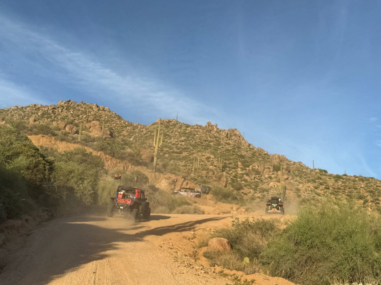 Off-road vehicles on dusty desert trail with cacti