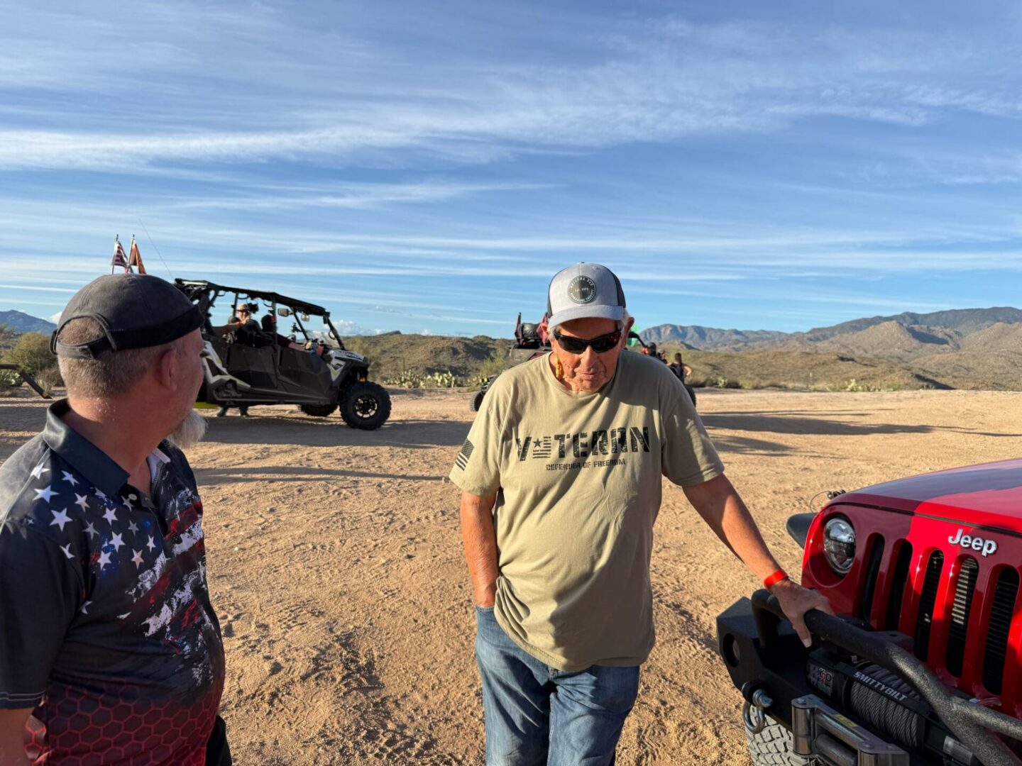 Two men leaning on red Jeep in desert