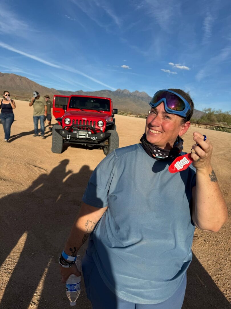 Smiling person wearing goggles near red Jeep