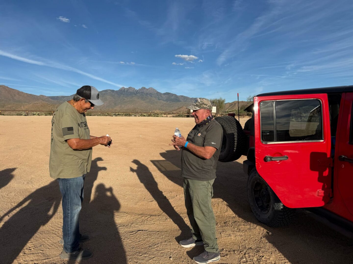 Two men talking beside red Jeep in desert