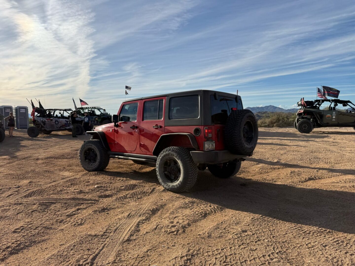 Red Jeep Wrangler parked in desert with UTVs