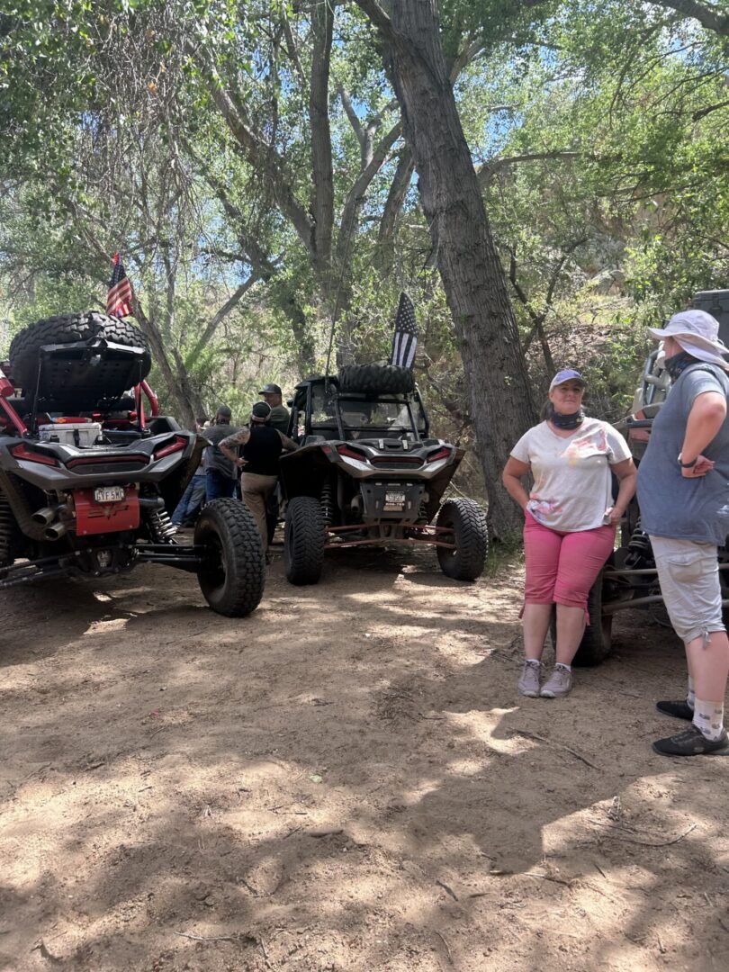 People with ATVs parked under leafy trees