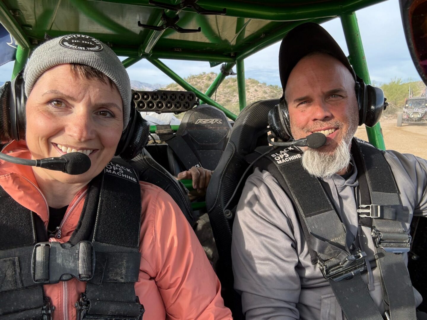 Two smiling people with headsets in off-road buggy