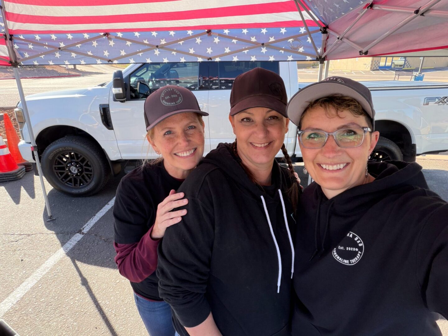 Three smiling people under American flag canopy