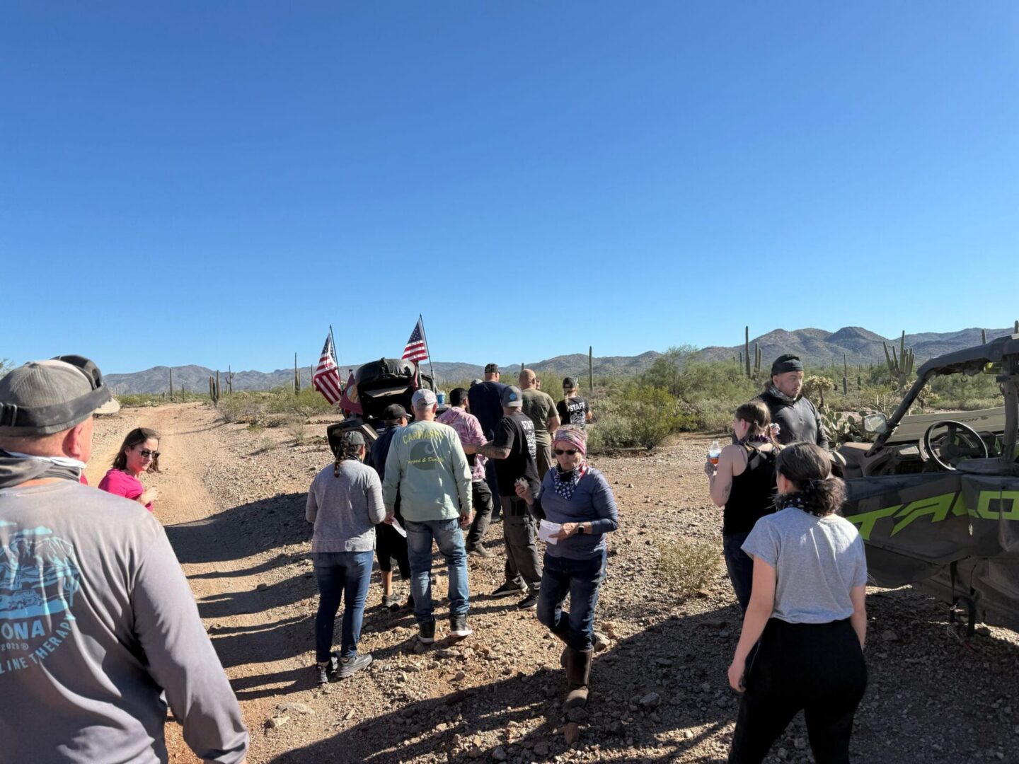 Group walking on desert trail with off-road vehicles