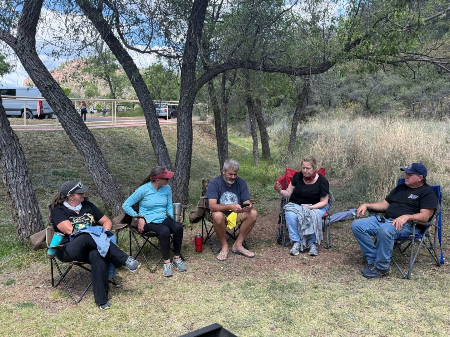 Five people chatting in camping chairs under trees